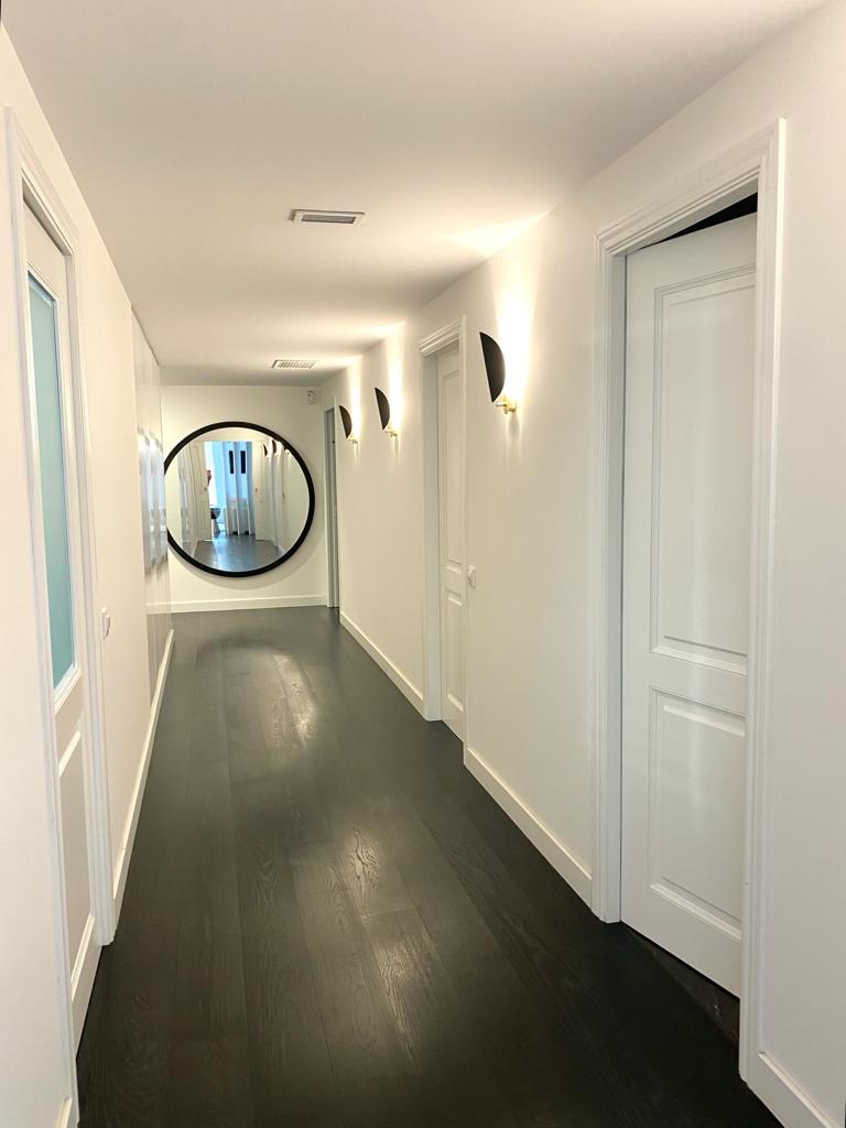 Pasillo con molduras blancas, zócalo y parquet oscuro en piso reformado en Barcelona